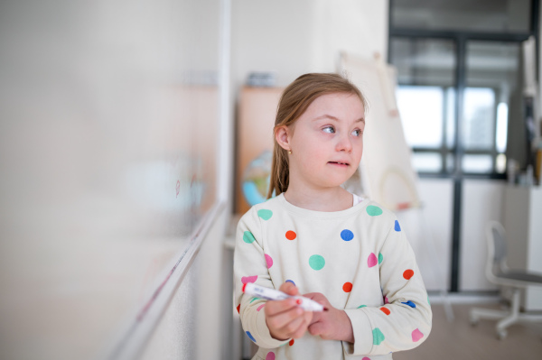 A little schoolgirl with down syndrome standing in front of whiteboard