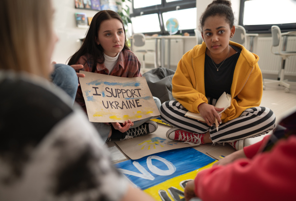 Teenage students sitting at circle in a classroom with posters to support Ukraine, no war concept.