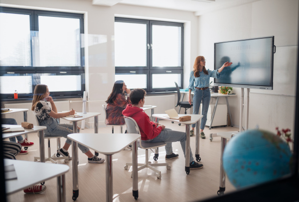 Happy young High school teacher giving marketing lesson to students in classroom