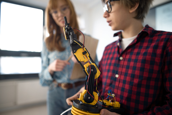 A college student presenting his builded robotic toy to young science teacher at robotics classroom at school.