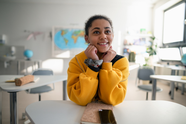 Happy college student sitting in school-desk and looking in camera.