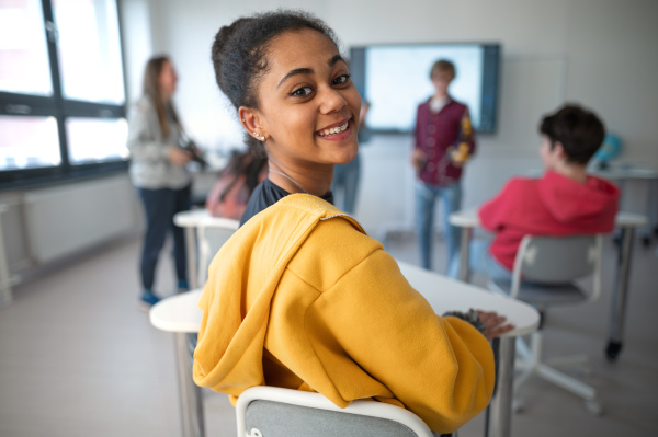 Happy college student sitting in school-desk and looking in camera.