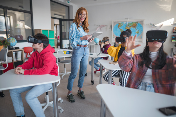 Young high school teacher giving lesson to students with VR goggles in a classroom