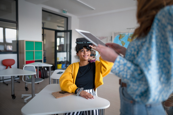 Young high school teacher giving lesson to students with VR goggles in a classroom