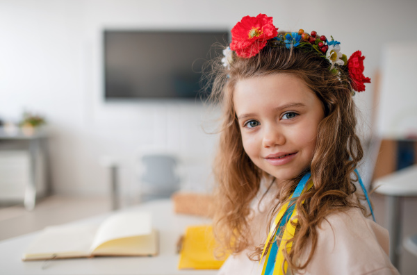 A little happy Ukrainian girl looking at camera in classroom, concept of enrolling Ukrainian kids to schools.