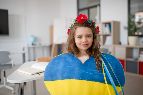 A little Ukrainian schoolgirl holding heart in Ukrainian colors and looking at camera at school.