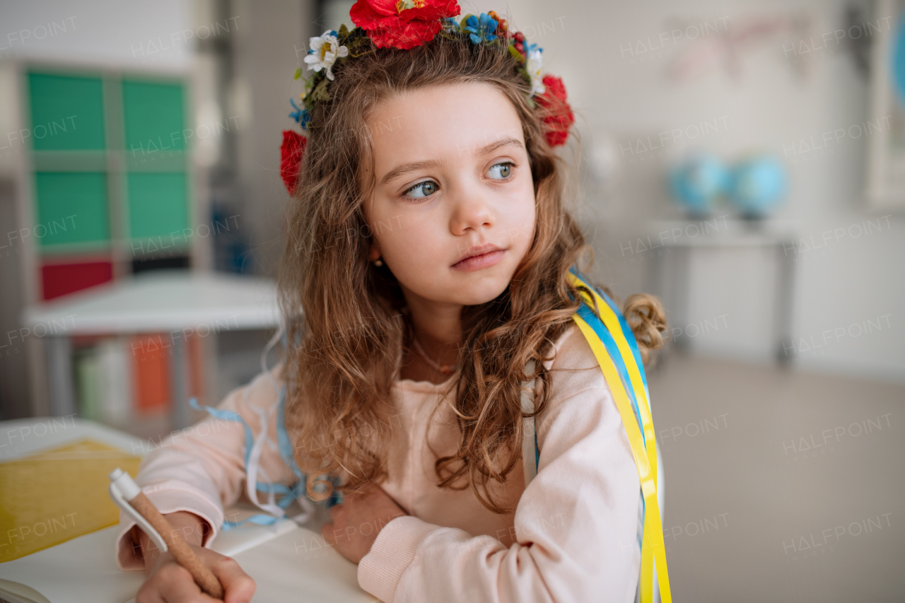 A little sad Ukrainian girl sitting in classroom during class, concept of enrolling Ukrainian kids to schools.