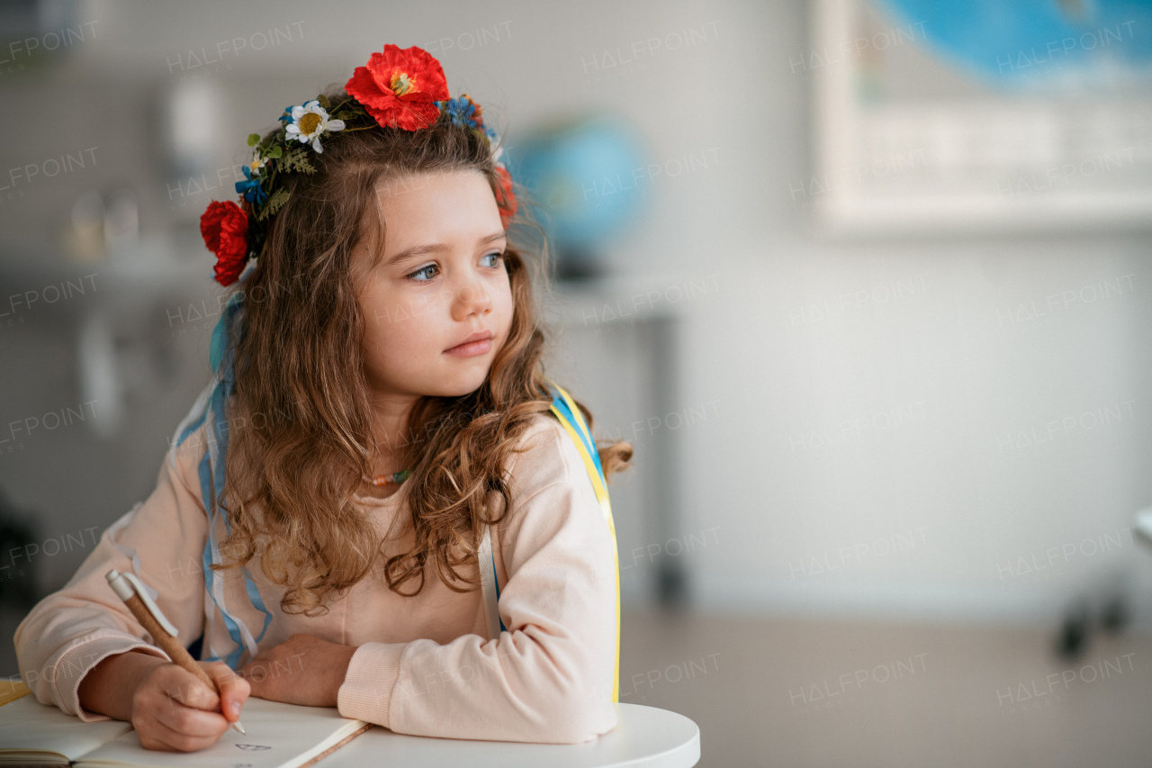 A little sad Ukrainian girl sitting in classroom during class, concept of enrolling Ukrainian kids to schools.