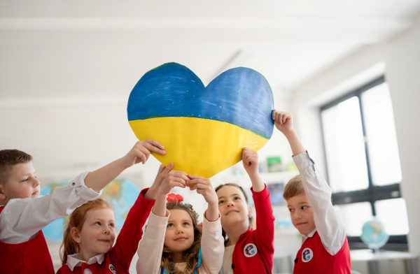 Little schoolchildren holidng a heart in Ukrainian colors in classroom, no war concept.