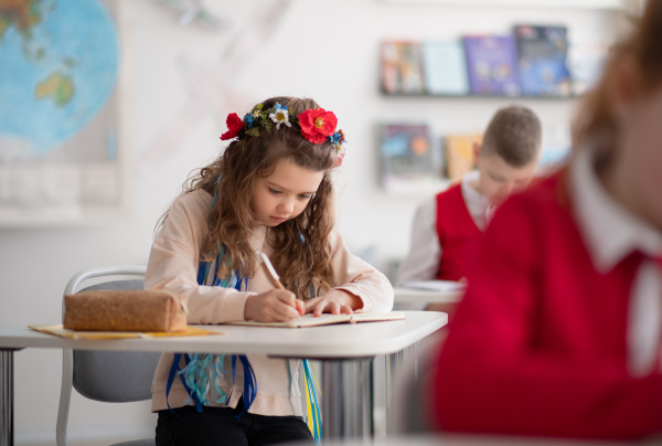 A little sad Ukrainian girl writing in classroom during class, concept of enrolling Ukrainian kids to schools.