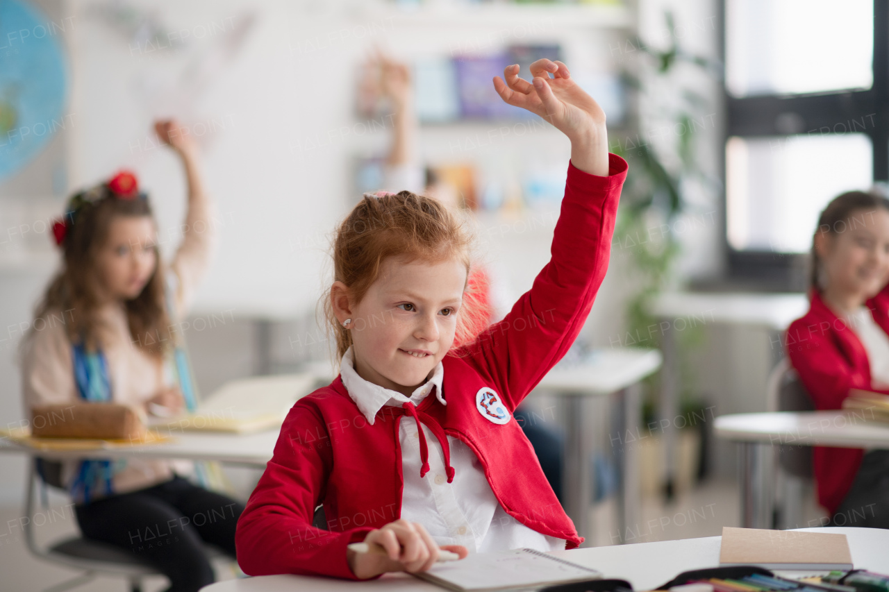 A happy schoolgirl with hands up during lesson in classroom at primary school.