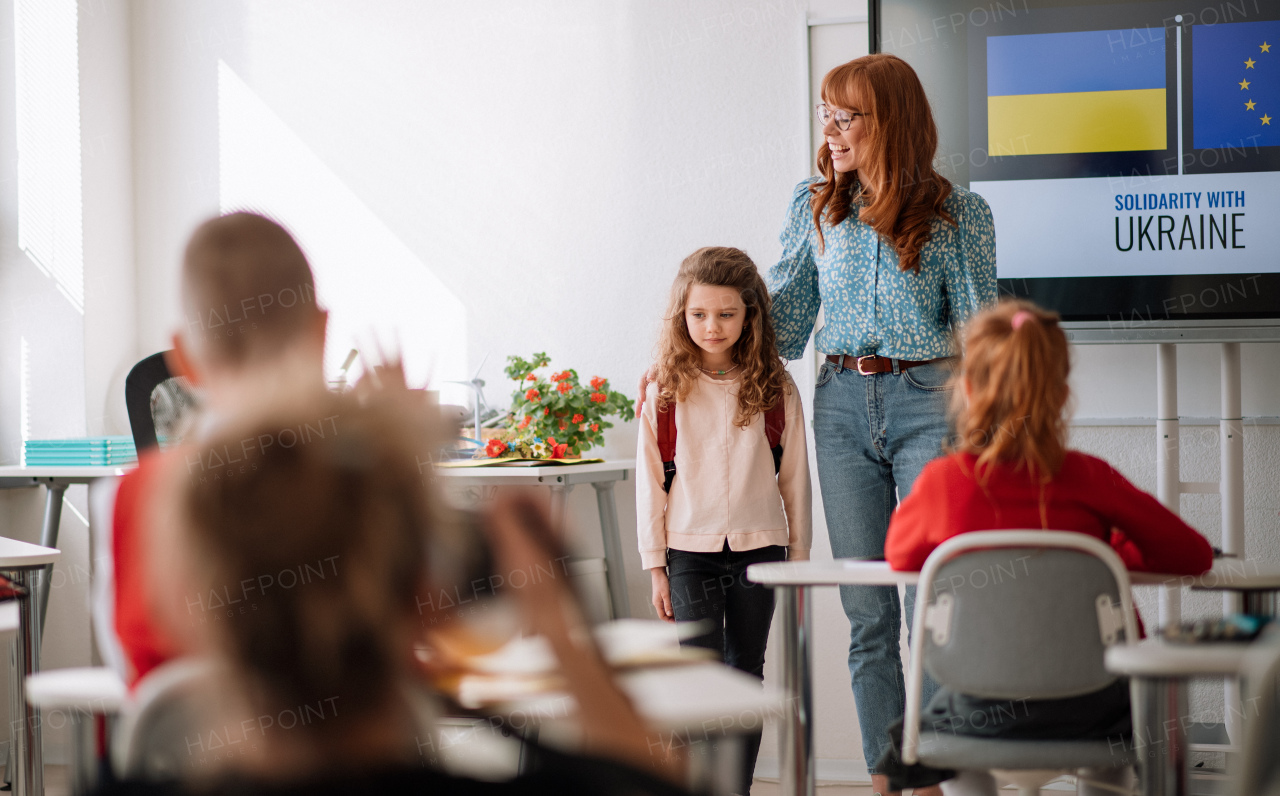 A teacher with Ukrainian schoolgirl in classroom, concept of enrolling and accpeting Ukrainian kids to schools.