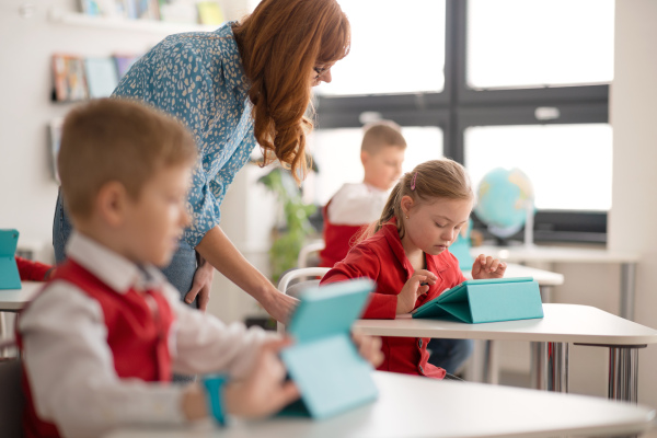 A schoolgirl with down syndrome using digital tablet during lesson in classroom at primary school. Integration concept.