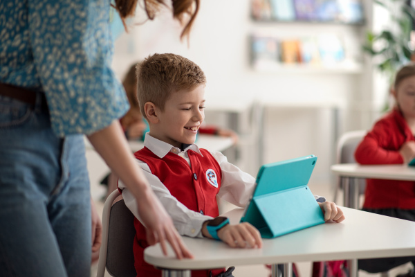 A happy schoolboy using digital tablet during lesson in classroom at primary school.