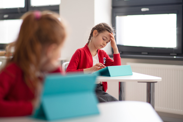 A bored schoolgirl using digital tablet during lesson in classroom at primary school.