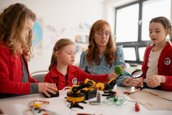 A group of kids with young science teacher programming electric toys and robots at robotics classroom