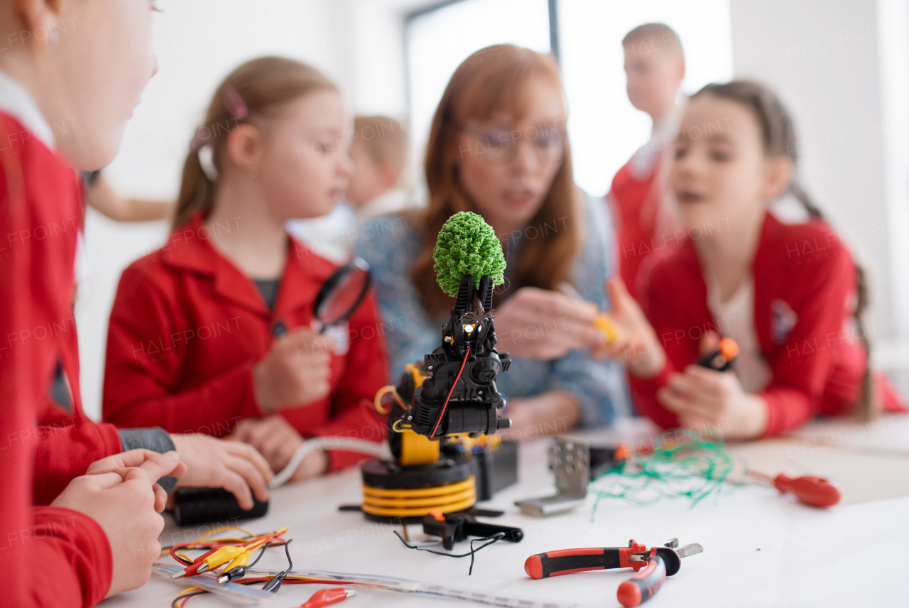 A group of kids with young science teacher programming electric toys and robots at robotics classroom