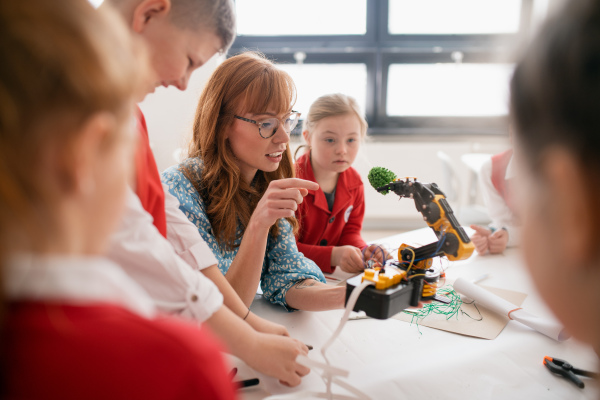 A group of kids with young science teacher programming electric toys and robots at robotics classroom