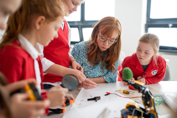 A group of kids with young science teacher programming electric toys and robots at robotics classroom