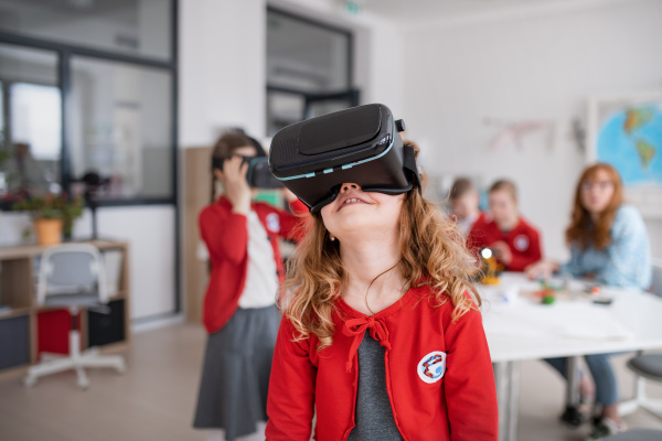 A happy schoolgirl wearing virtual reality goggles at school in computer science class