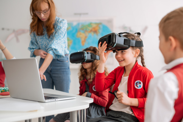 Happy schoolchildren wearing a virtual reality goggles at school in computer science class