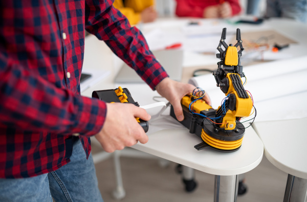 College student engineering his builded robotic toy in a science robotics classroom at school. Close-up.