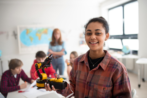 A college student holding her robotic toy at robotics classroom at school.