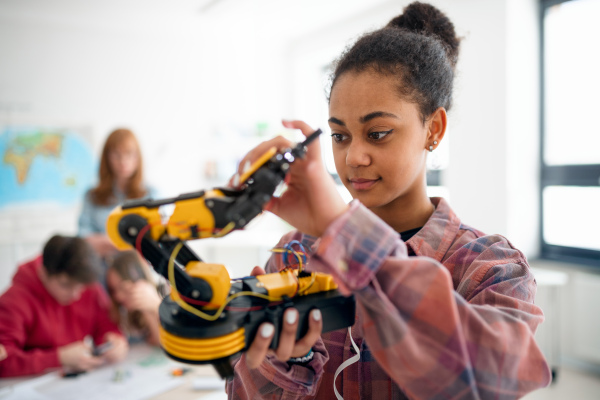 A college student holding her robotic toy at robotics classroom at school.