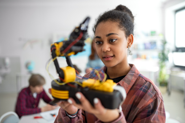 A college student holding her robotic toy at robotics classroom at school.