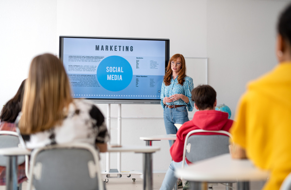 Happy young High school teacher giving marketing lesson to students in classroom