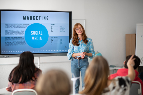 A young High school teacher giving marketing lesson to students in classroom