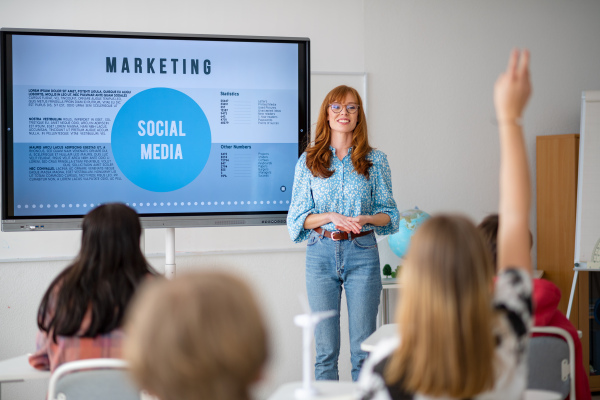 A young High school teacher giving marketing lesson to students in classroom