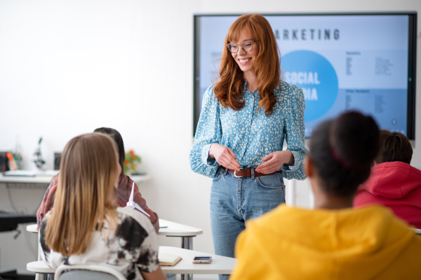 A young High school teacher giving marketing lesson to students in classroom