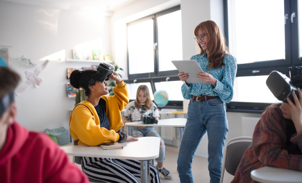 Happy young High school teacher giving lesson to students with VR glasses in classroom