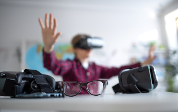 A happy student wearing virtual reality goggles at school in computer science class, close-up at glasses.