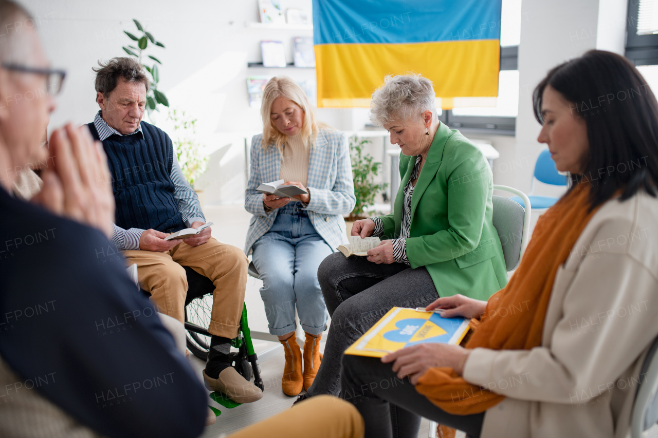 A group of seniors praying for Ukraine together in church community center.