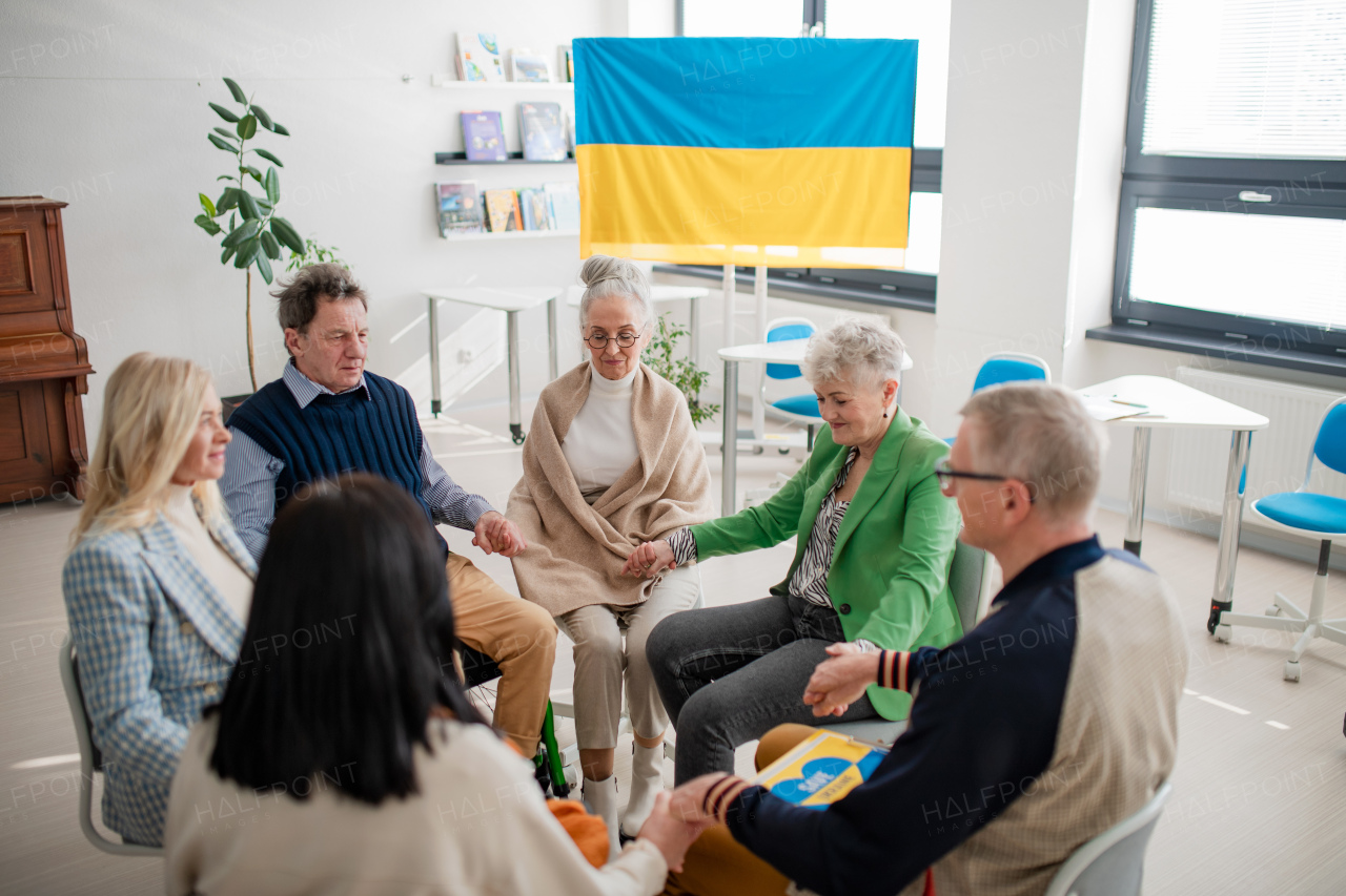 A group of seniors holding hands and praying for Ukraine together in church community center.