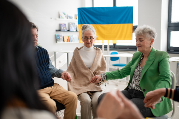 A group of seniors holding hands and praying for Ukraine together in church community center.