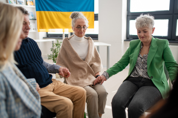 A group of seniors holding hands and praying for Ukraine together in church community center.