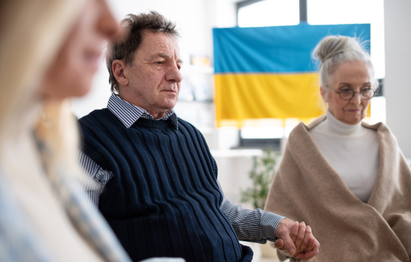 A group of seniors holding hands and praying for Ukraine together in church community center.