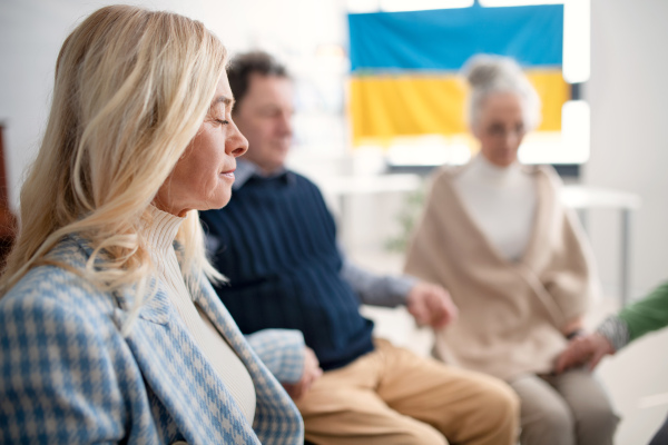 A group of seniors holding hands and praying for Ukraine together in church community center.