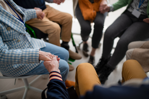 A group of seniors holding hands and praying for Ukraine together in church community center, close-up.