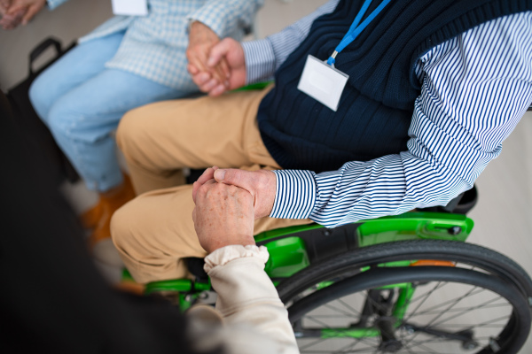 A close-up of senior man sitting in wheelchair at group therapy session.