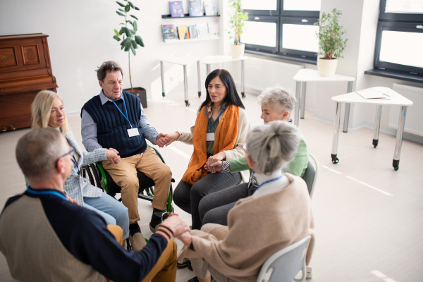 A group of senior people sitting in circle during therapy session, holding hands and praying together.