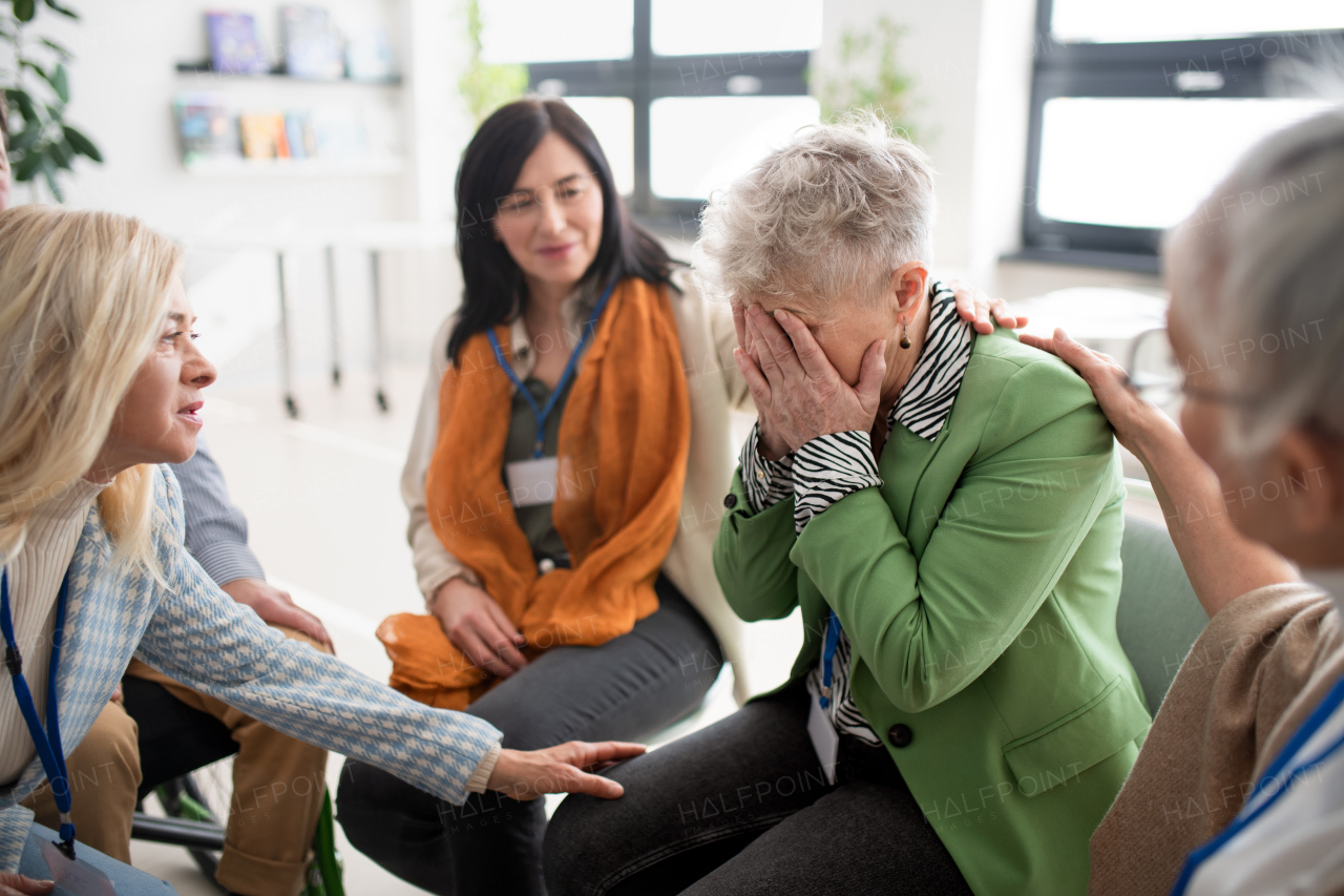 A group of senior people sitting in circle during therapy session, consoling depressed woman.