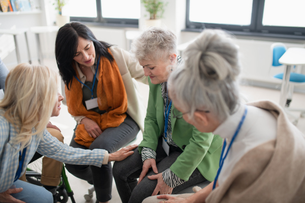 A group of senior people sitting in circle during therapy session, consoling depressed woman.