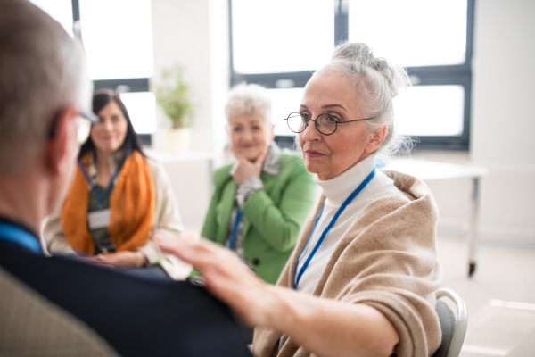 A group of senior people sitting in circle during therapy session, woman consoling depressed man.