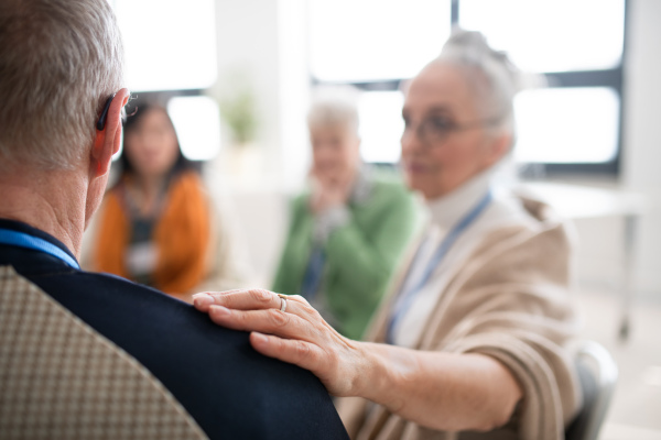 A group of senior people sitting in circle during therapy session, woman consoling depressed man.