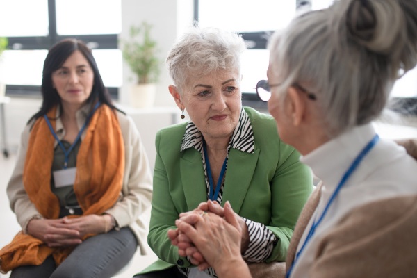 A group of senior people sitting in circle during therapy session, consoling depressed woman.