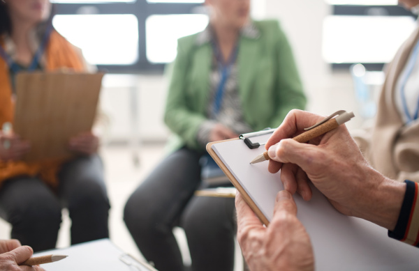 Elderly people attending a group therapy session at nursing house, sitting in circle, having conversation with psychologist, close-up